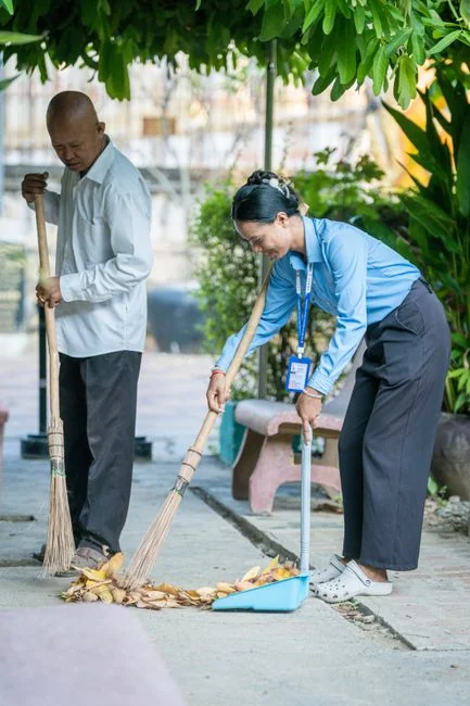 services-01 A man cleaning a glass barrier outdoors with a squeegee, surrounded by greenery.